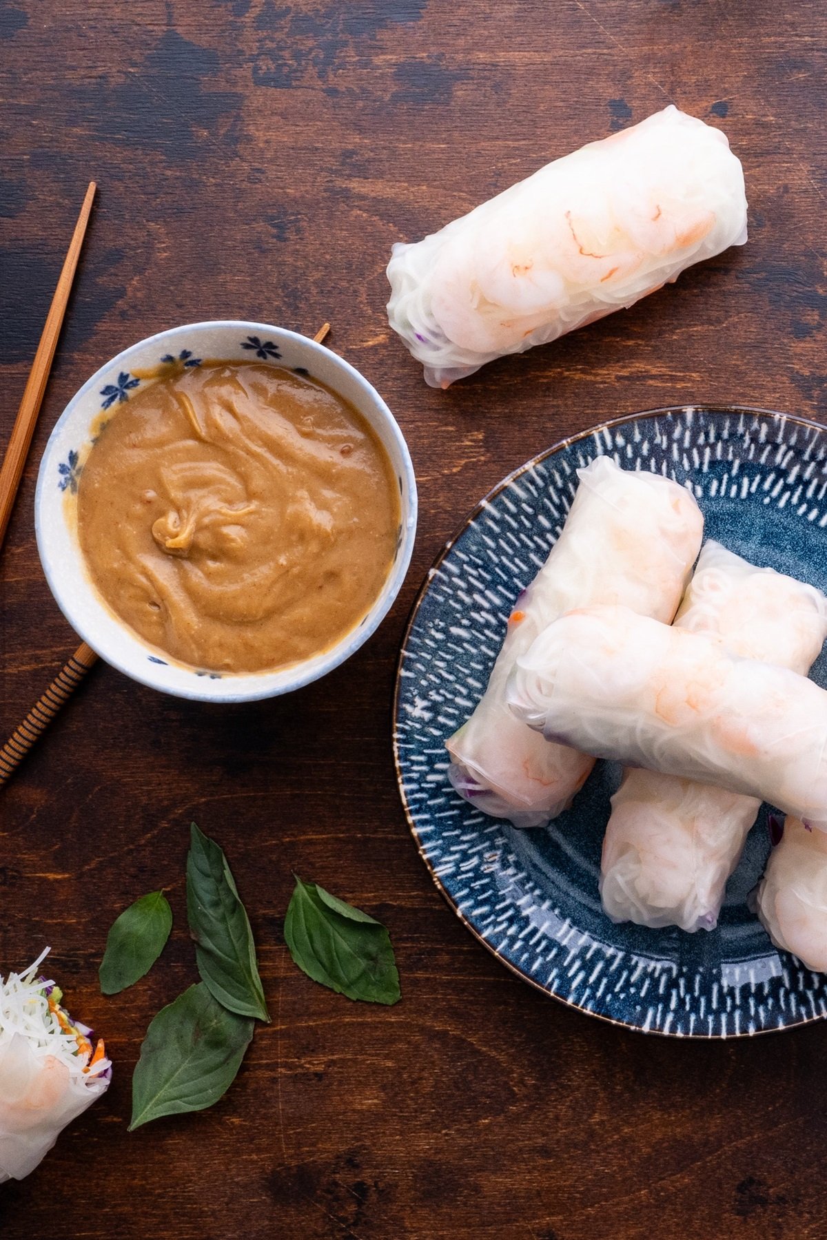 Blue plate with Spring rolls on top and a bowl of peanut dipping sauce to the side.