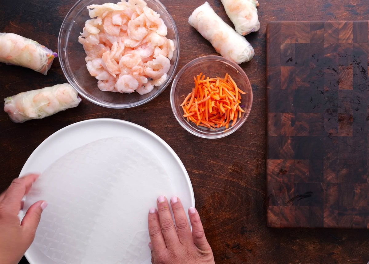 Hands placing spring roll wrapper in hot water to rehydrate it.