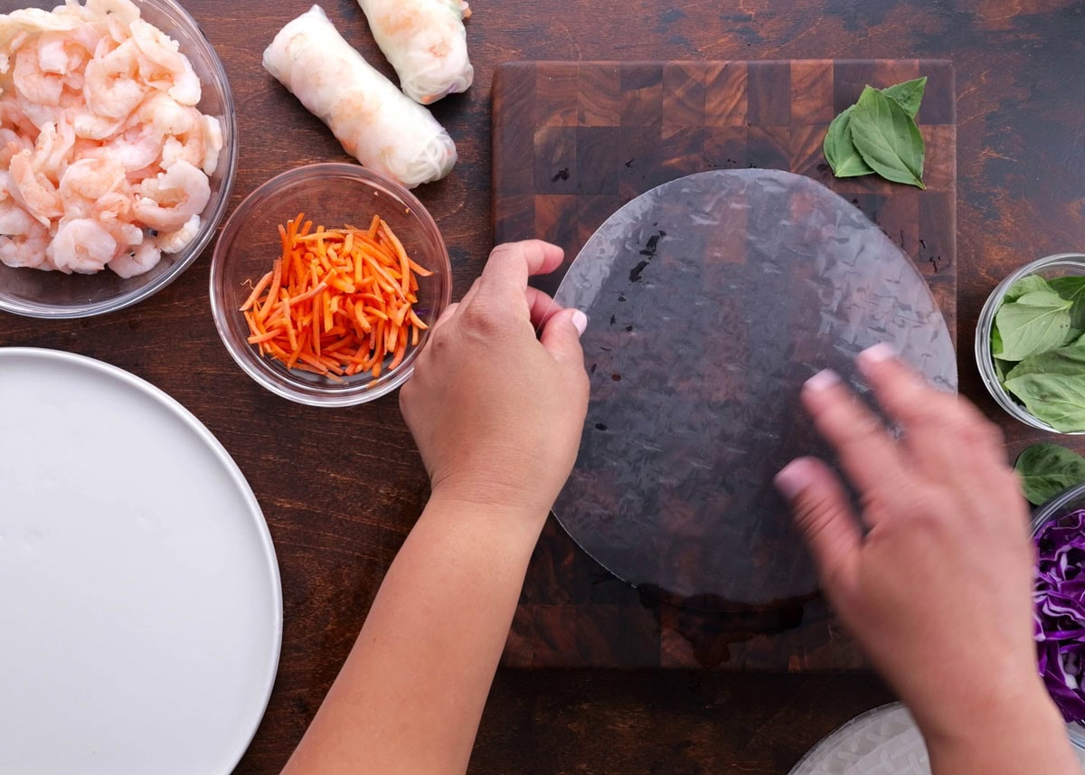 Hands laying a rehydrated rice wrapper on a cutting board.