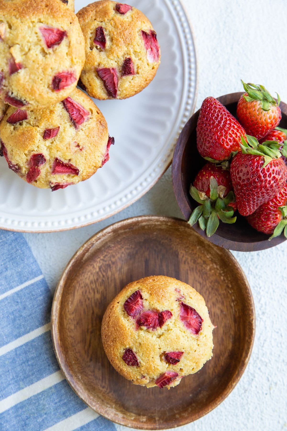 One large plate of strawberry muffins and one small wooden plate with one strawberry muffin