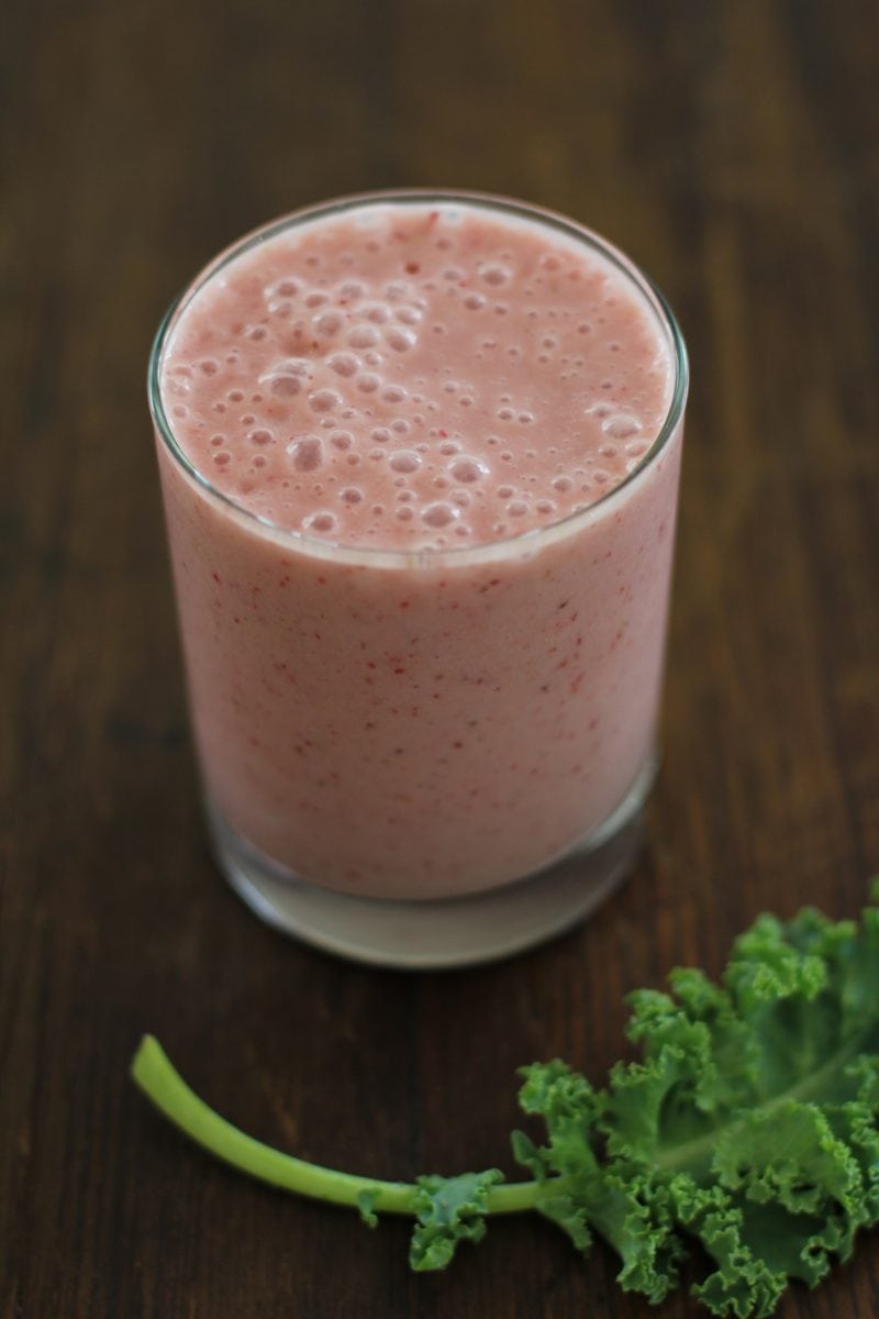 Glass of strawberry banana smoothie with a kale leaf to the side.