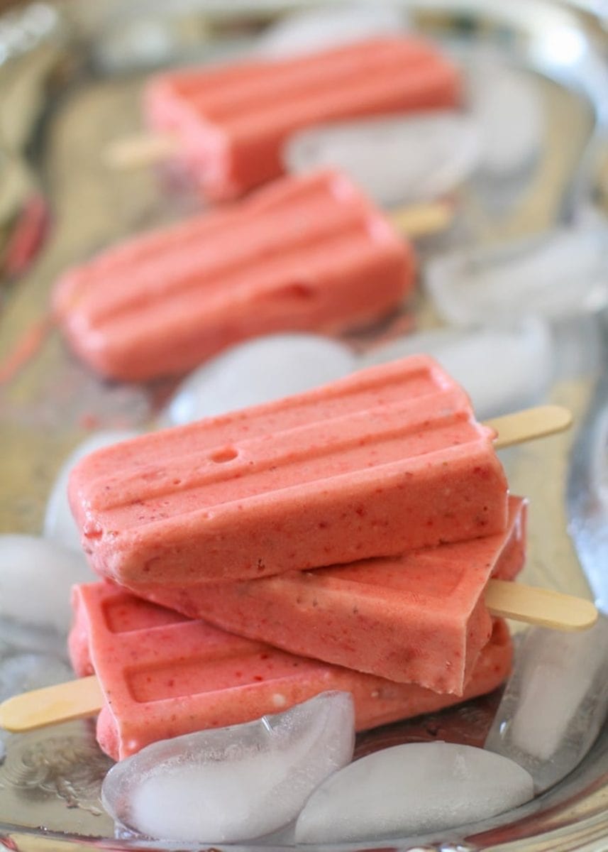 Stack of strawberry coconut milk popsicles on a silver tray with ice cubes, ready to eat.