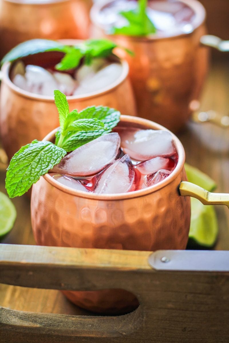 Strawberry Moscow mules in a wooden serving tray with fresh lime leaves, ready to serve.
