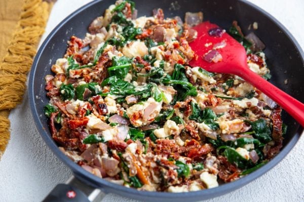 Onion, sun-dried tomatoes, spinach and feta cheese in a skillet. To be used as topping for the salmon.