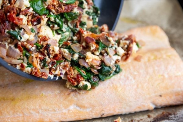 Pouring the sun-dried tomato feta mixture over the salmon filet.