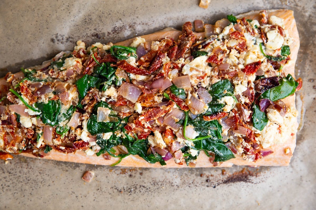 Salmon with sun-dried tomatoes, onion, spinach and feta on top, ready to go into the oven.