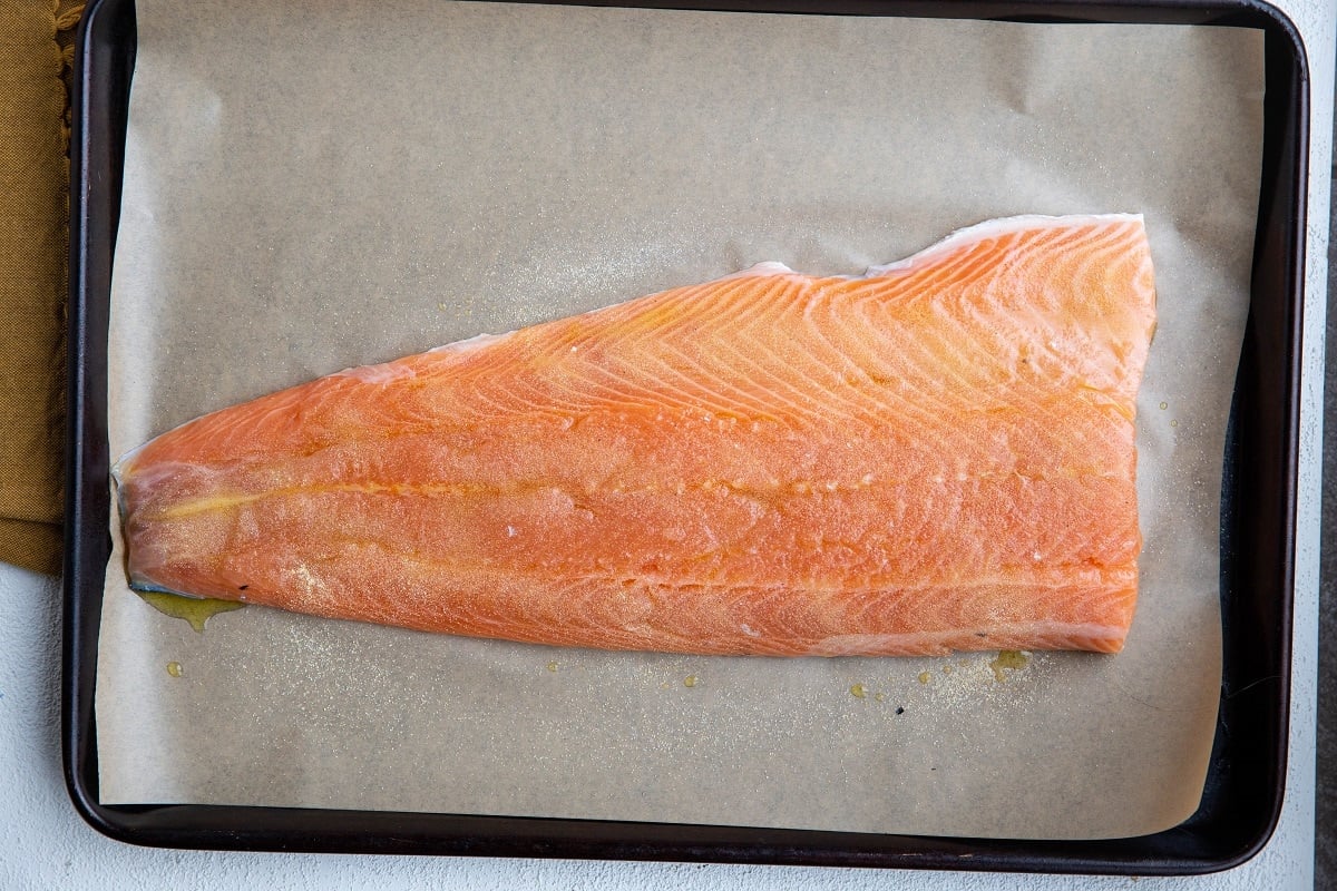 large salmon filet on a baking sheet with oil, salt and garlic powder on top.