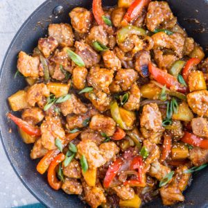 Large skillet full of cooked sweet and sour pork with a blue napkin to the side.