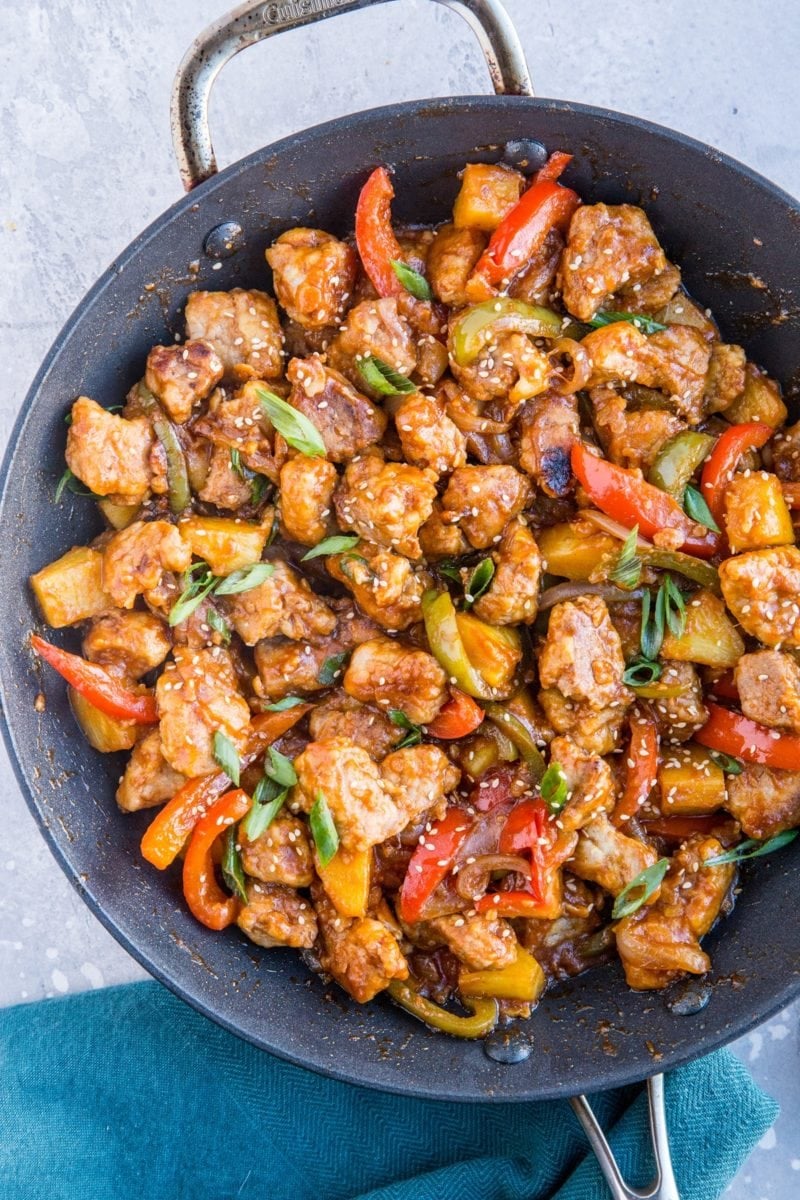 Large skillet full of cooked sweet and sour pork with a blue napkin to the side.