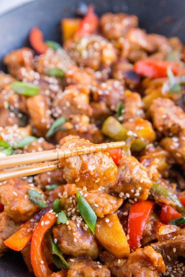Sweet and Sour Pork in a large skillet with chop sticks taking a bite of pork.