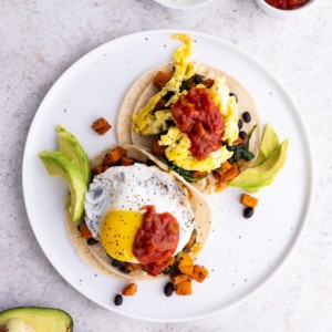 Plate of sweet potato and black bean breakfast tacos with eggs and avocado on top, ready to eat.