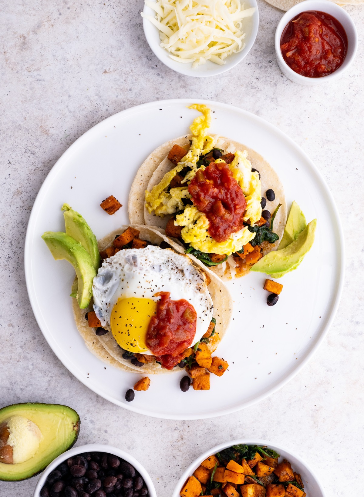 Plate of sweet potato and black bean breakfast tacos with eggs and avocado on top, ready to eat.