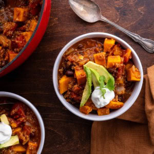 Sweet Potato black bean quinoa chili in two bowls with topping. A spoon and napkin to the side, ready to serve.