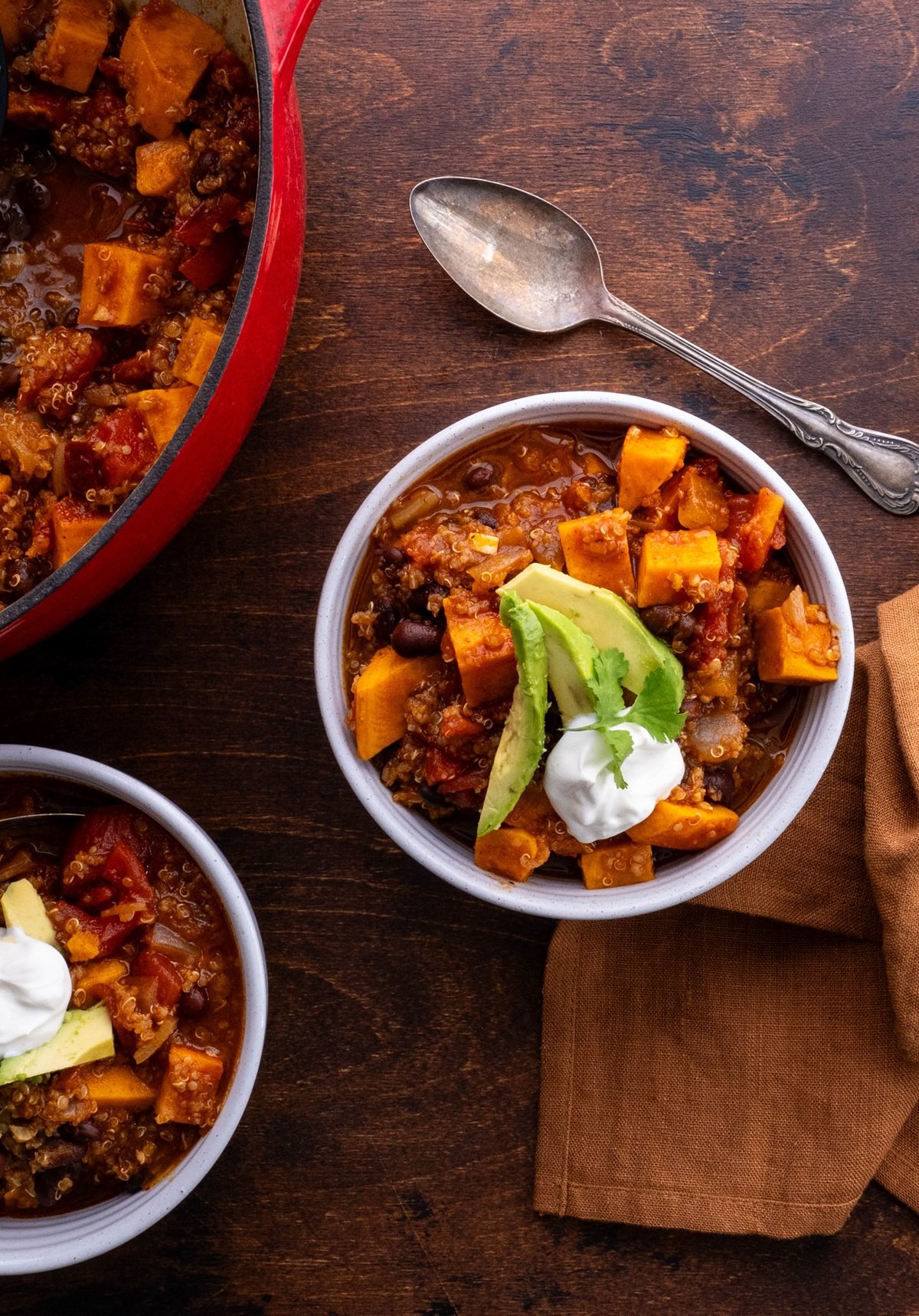 Sweet Potato black bean quinoa chili in two bowls with topping. A spoon and napkin to the side, ready to serve.