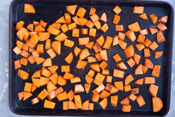 Raw seasoned sweet potatoes spread across a baking sheet, ready to roast.