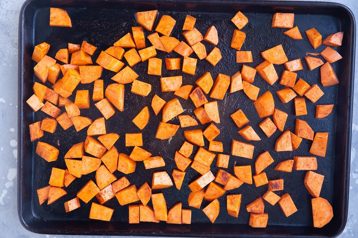 Raw seasoned sweet potatoes spread across a baking sheet, ready to roast. 