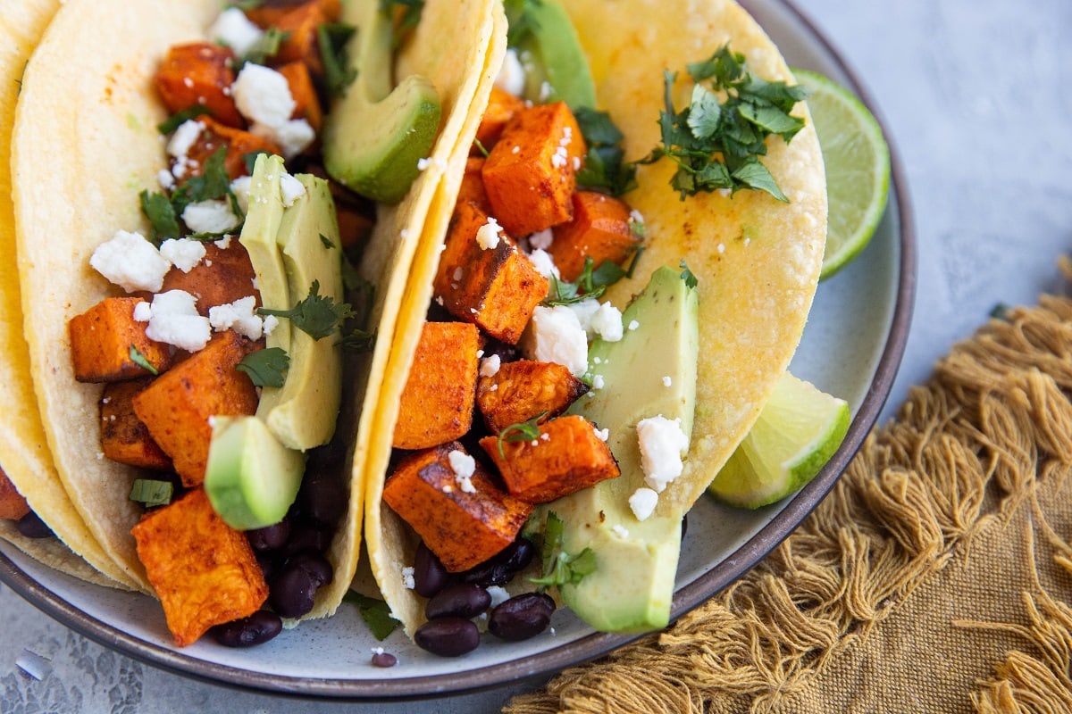 Sweet potato and black bean tacos on a plate with cheese and cilantro sprinkled on top. Amazing vegetarian tacos.