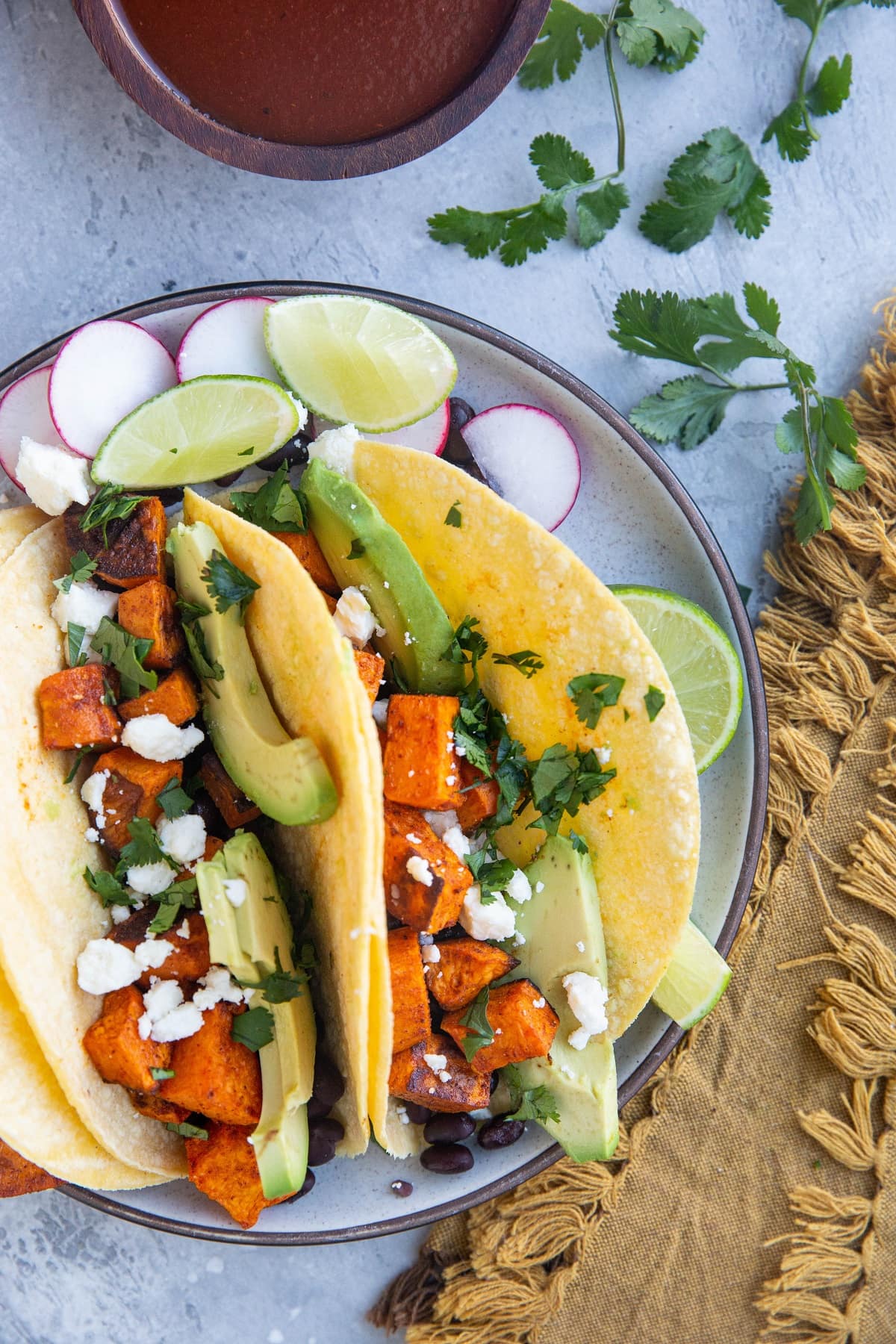 Plate of three sweet potato and black bean tacos with enchilada sauce to the side for dipping. Amazing veggie tacos!