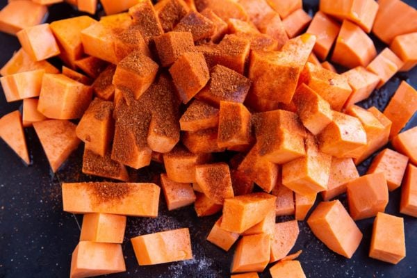 Pile of chopped sweet potatoes and seasonings on a sheet pan.