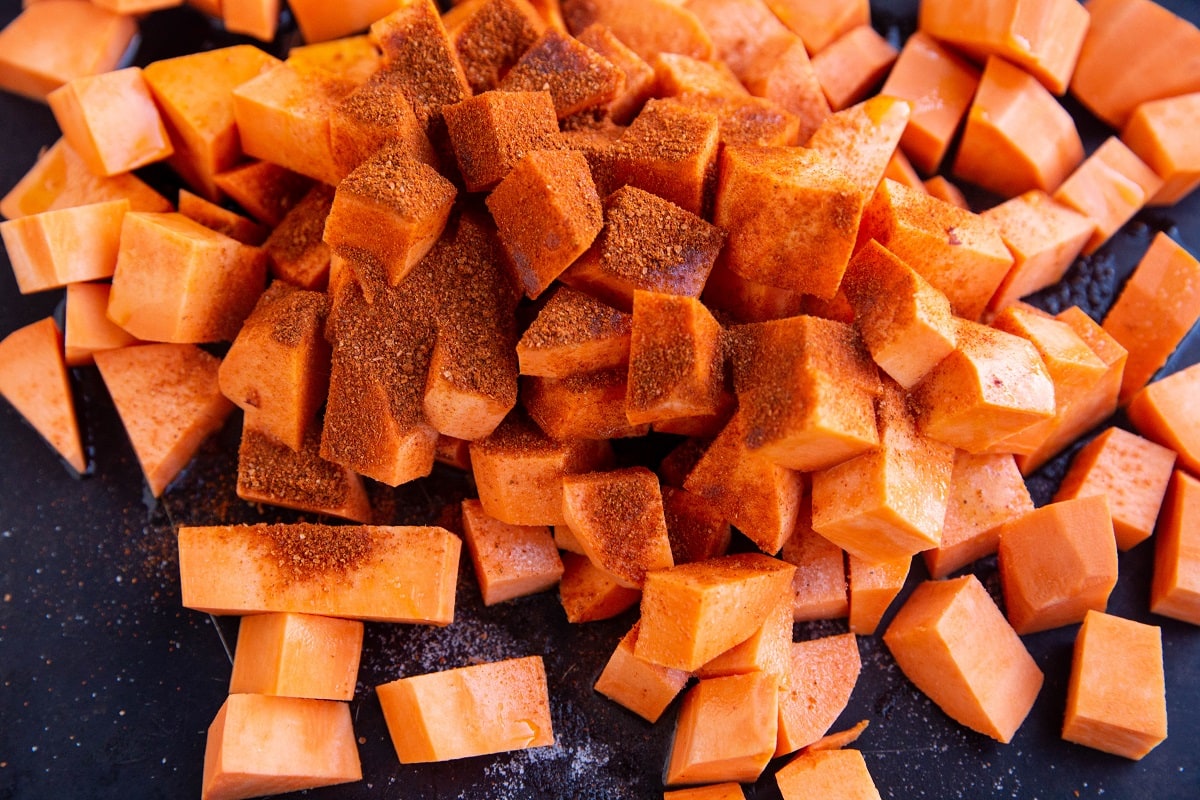 Pile of chopped sweet potatoes and seasonings on a sheet pan to make vegetarian tacos.