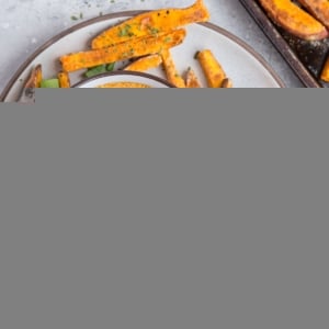 Sweet potato fries on a plate with a bowl of chipotle dipping sauce in the center, sprinkled with green onions. Ready to serve.