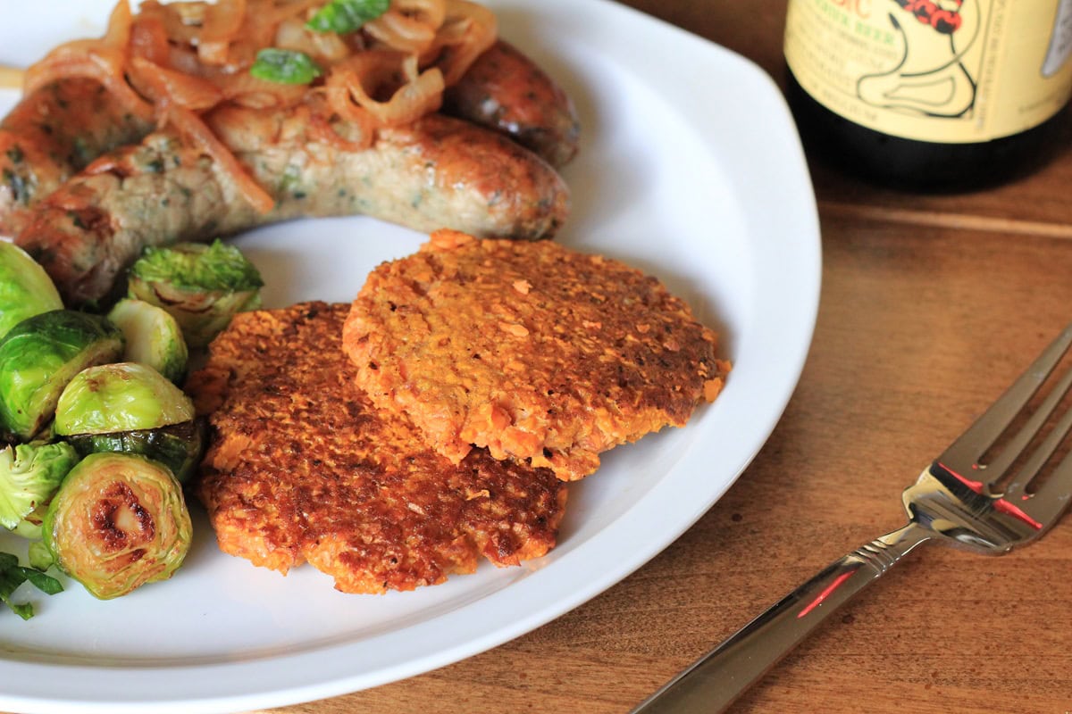 sweet potato rosti (hash browns) on a plate with sausage and brussel sprouts with a fork to the side, ready to serve.