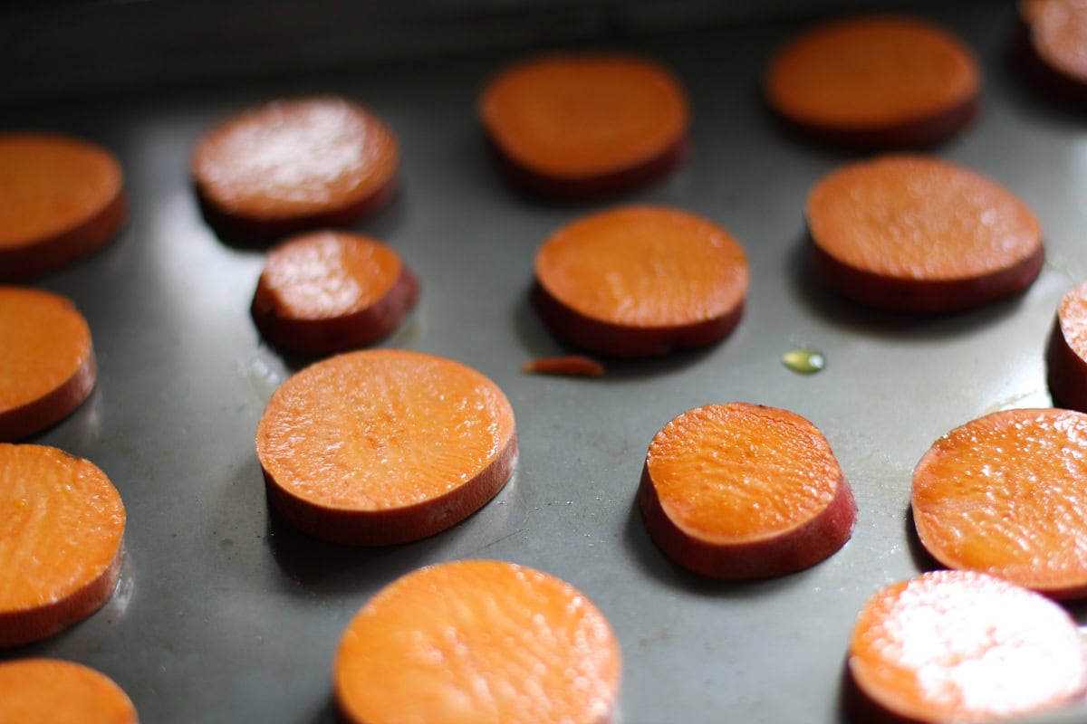 Slices of sweet potatoes covered with a layer of oil on a baking sheet ready to go into the oven.