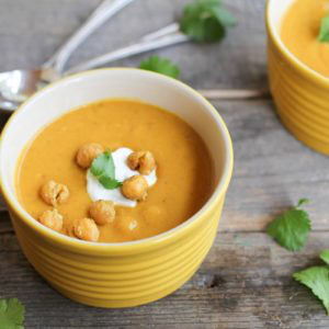 Roasted sweet potato soup in a yellow ramekin with roasted chickpeas and yogurt on top, ready to serve.