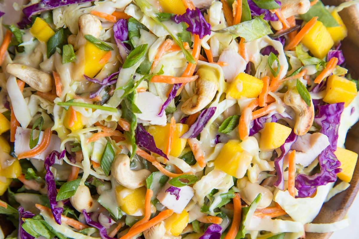 A big wood bowl full of Thai Chicken Chopped Salad with cabbage, cashews, mango, and peanut dressing.