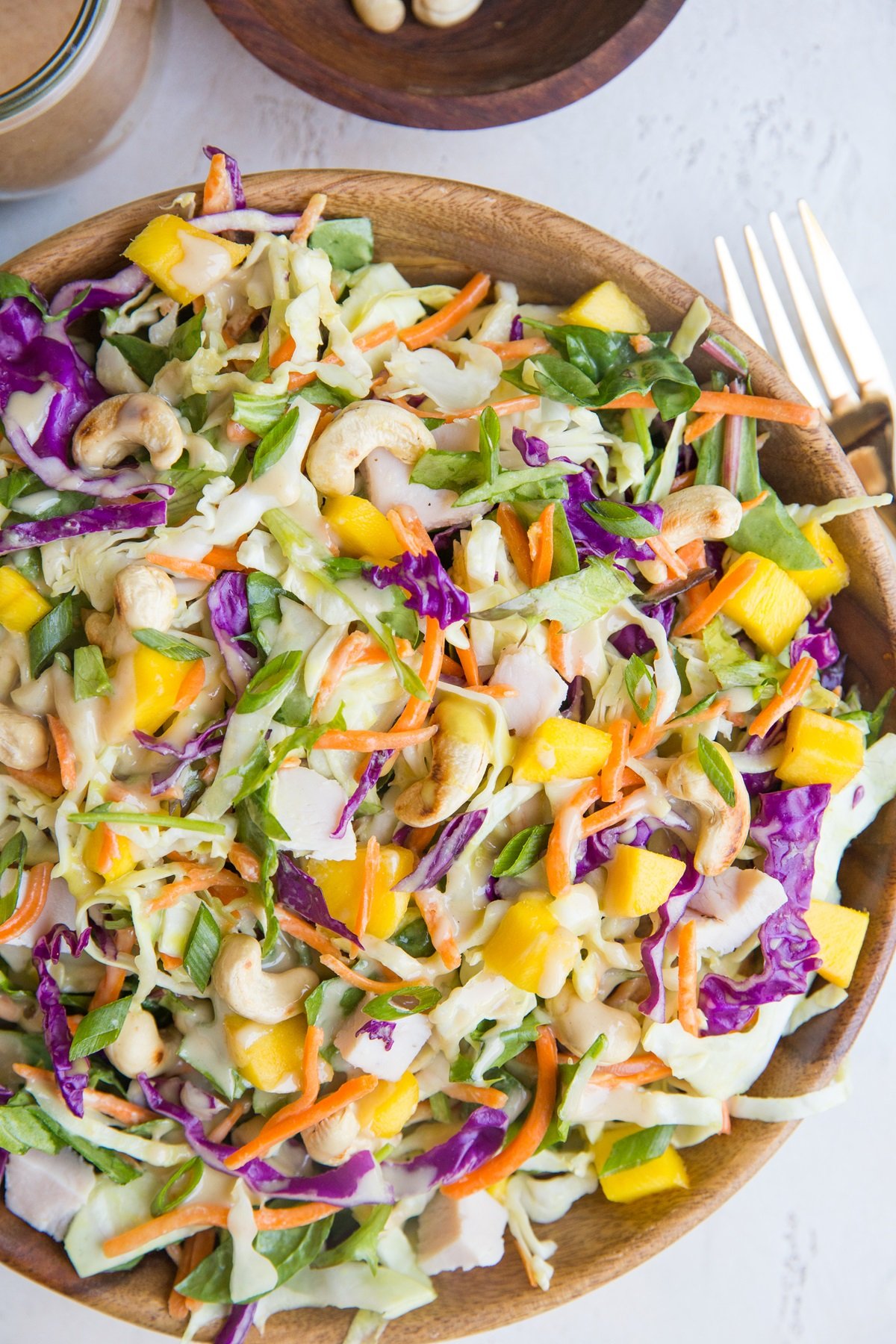 Wooden bowl full of Thai Chicken Chopped Salad with cabbage, cashews, mango, and peanut dressing.