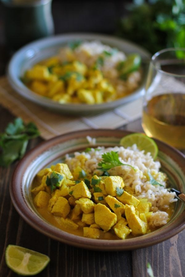 Yellow Thai curry in a bowl with brown rice and fresh limes and cilantro. on a wooden table.