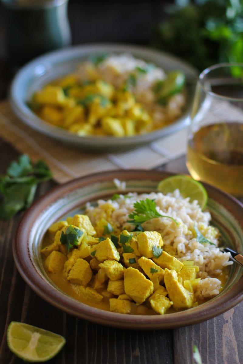 Yellow Thai curry in a bowl with brown rice and fresh limes and cilantro. on a wooden table.