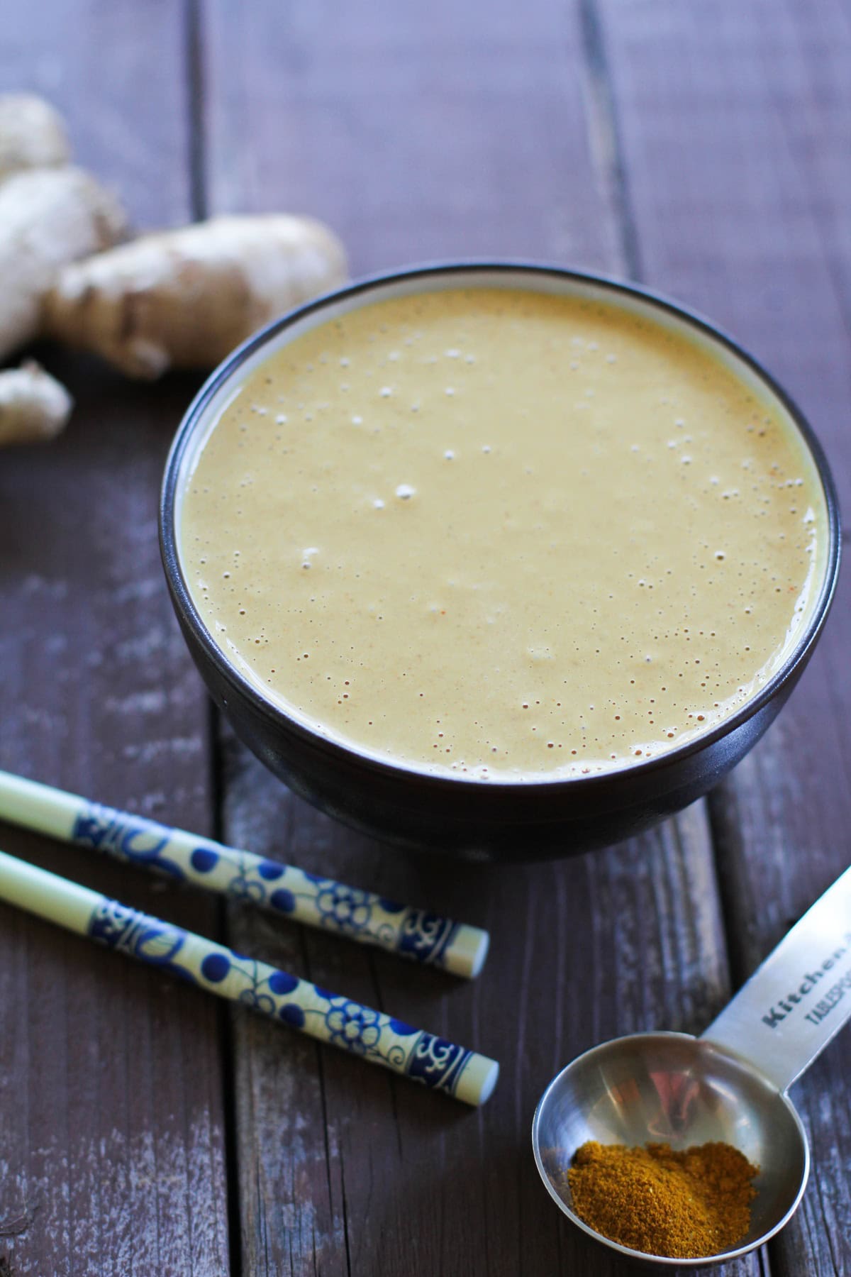 Peanut sauce in a bowl, ready to serve. Chop sticks, fresh ginger, and curry powder to the side.