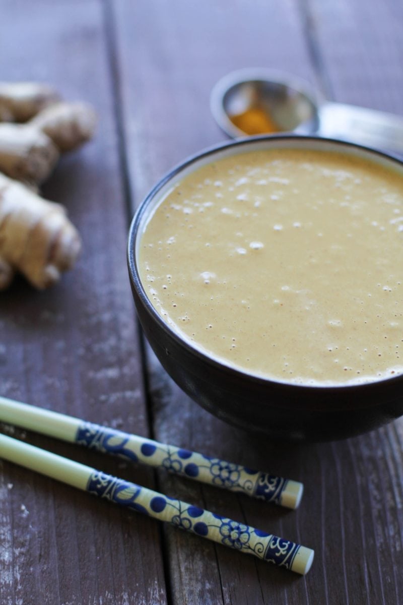 Thai Peanut Sauce in a bowl with chopsticks to the side and fresh ginger in the background.