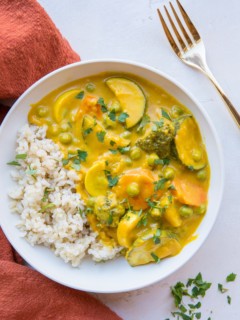 Vegan Pumpkin Curry in a white bowl with rice and a red napkin to the side.