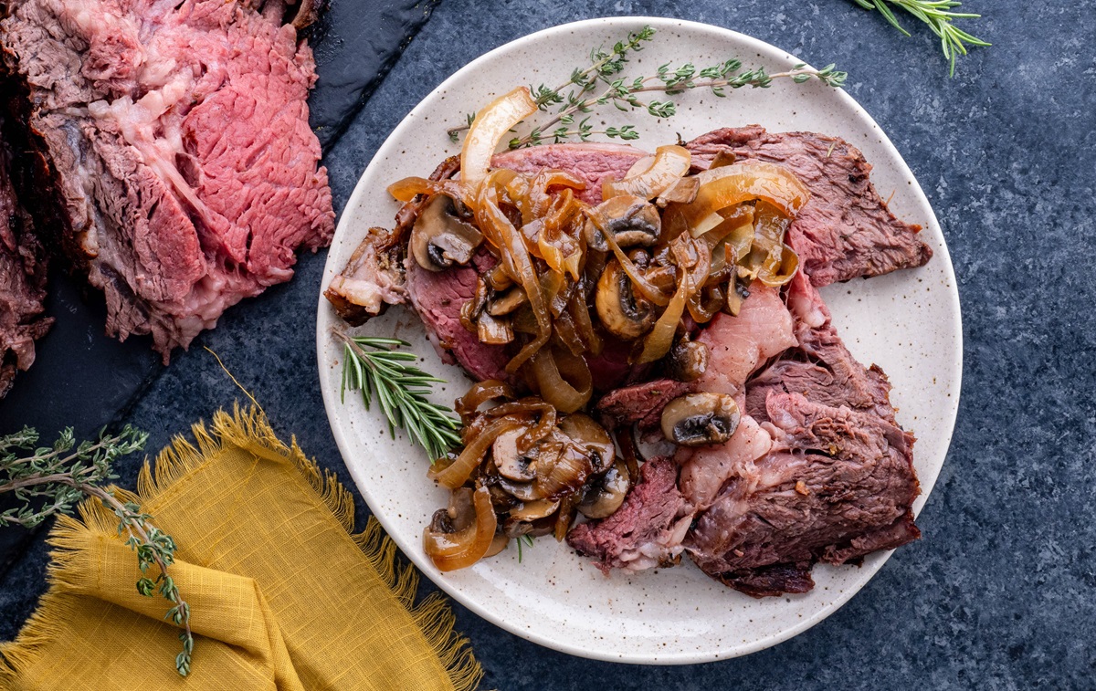 Plate of garlic butter prime rib with caramelized onions and mushrooms on top.