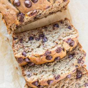 Loaf of gluten-free banana bread on a sheet of parchment paper, cut into slices.