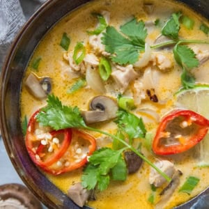 Tom kha gai soup in a big bowl, ready to serve. A fresh mushroom and a half of a lime next to the bowl of soup.