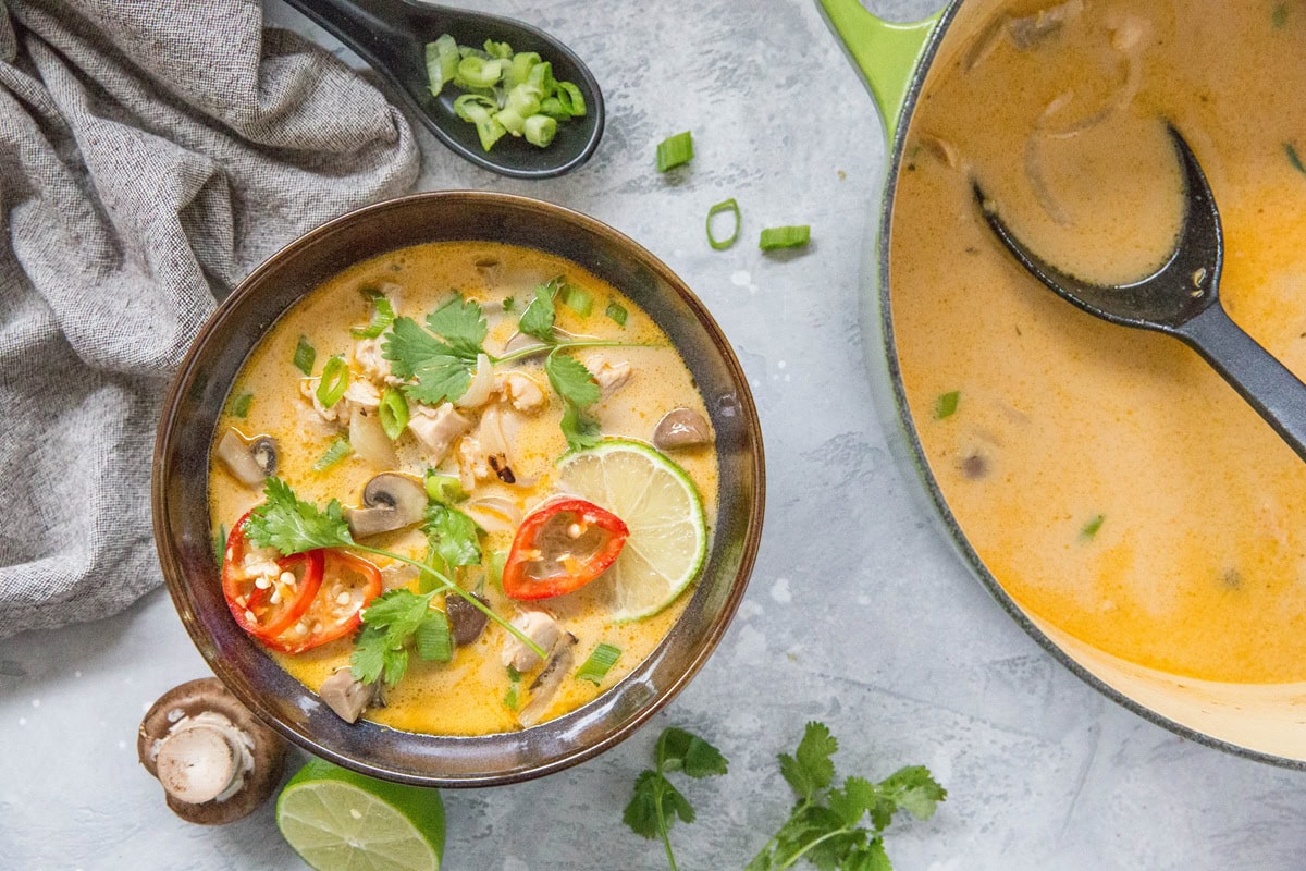 Bowl of Tom Kha Gai soup with the rest of the pot of soup to the side.