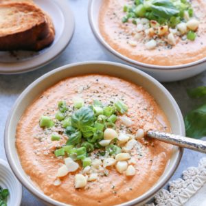 Creamy Vegan Tomato Basil Soup in two bowls with fresh basil on top and a cream colored napkin to the side.