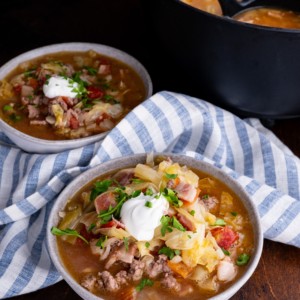 Sausage and cabbage stew in two bowls with a pot of soup in the background