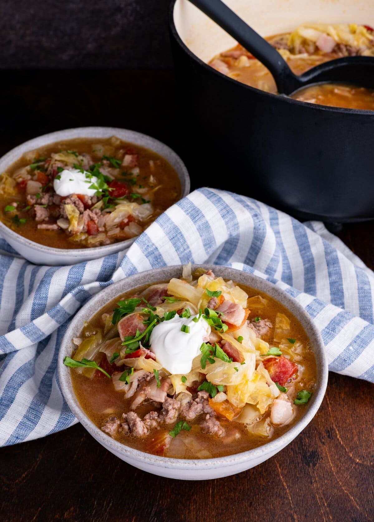 Sausage and cabbage stew in two bowls with a pot of soup in the background