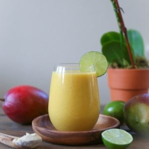 Immunity Boosting Tropical Smoothie sitting on a wooden plate on a wooden table with fresh mangoes in the background
