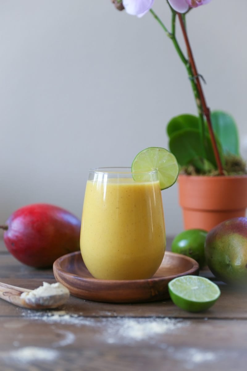 Immunity Boosting Tropical Smoothie sitting on a wooden plate on a wooden table with fresh mangoes in the background