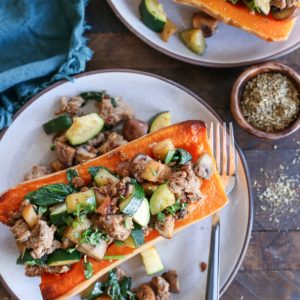 Two halves of butternut squash on two plates, stuffed with ground turkey, kale, mushrooms, zucchini, and more. Ready to serve.