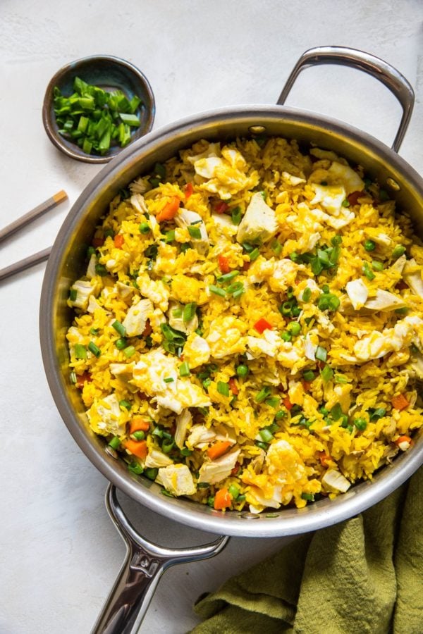 Turmeric Chicken Fried Rice in a stainless steel skillet with a green napkin to the side and a bowl full of chopped green onions.
