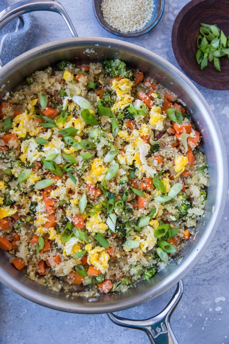Turnip fried rice in a stainless steel skillet with a napkin and a bowl of sesame seeds to the side.