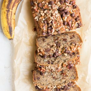 Loaf of vegan banana bread cut into individual slices with fresh ripe bananas to the side.