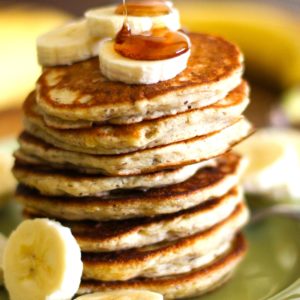 Gluten-Free Vegan Banana Pancakes on a green plate with sliced bananas on top with pure maple syrup being drizzled on top. Ready to eat.