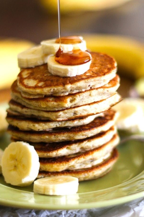 Gluten-Free Vegan Banana Pancakes on a green plate with sliced bananas on top with pure maple syrup being drizzled on top. Ready to eat.